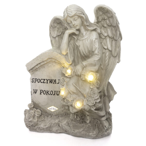 Figurka anioła z masy kamiennej oparta o nagrobek z napisem spoczywaj w pokoju